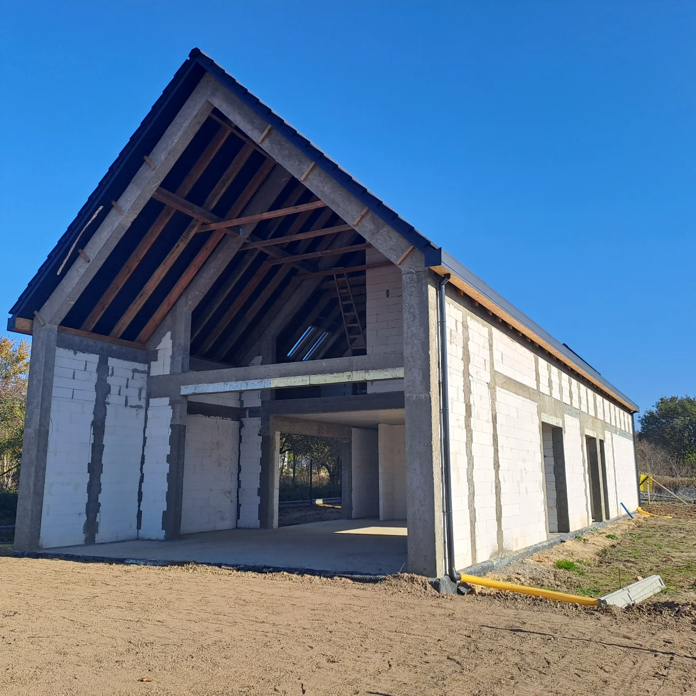 Stan surowy domu z odsłoniętą konstrukcją dachu i ścianami z białych bloczków gazobetonowych