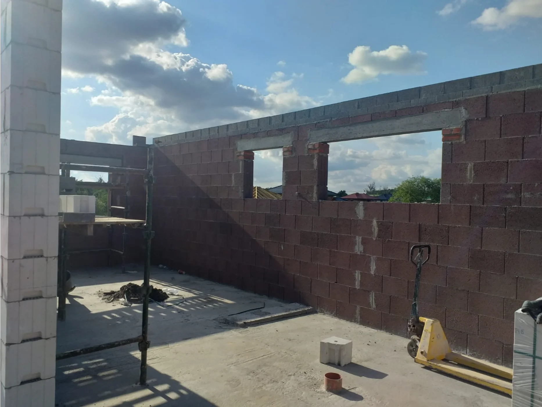 Stan surowy domu z murowanymi ścianami, otworami okiennymi, rusztowaniem na płycie fundamentowej