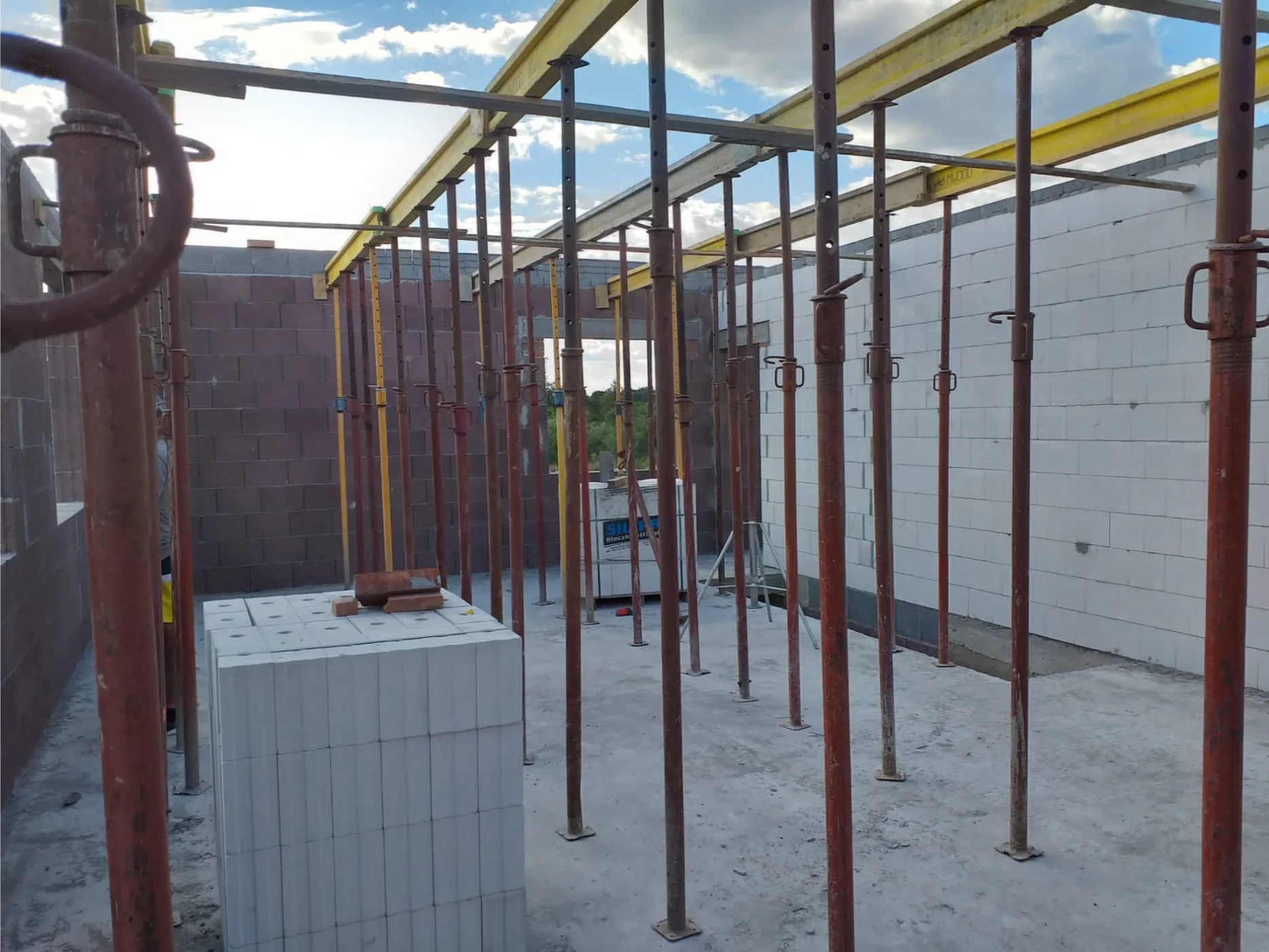 Wnętrze budowy w stanie surowym domu z podpórkami stropowymi i bloczkami gazobetonowymi