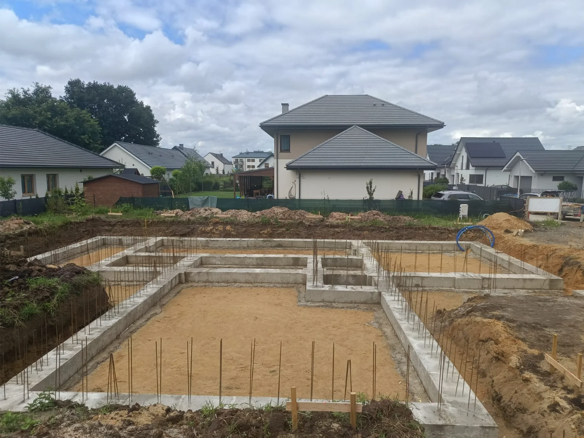 Widok na wykonaną płytę fundamentową z zbrojeniem na tle istniejących domów