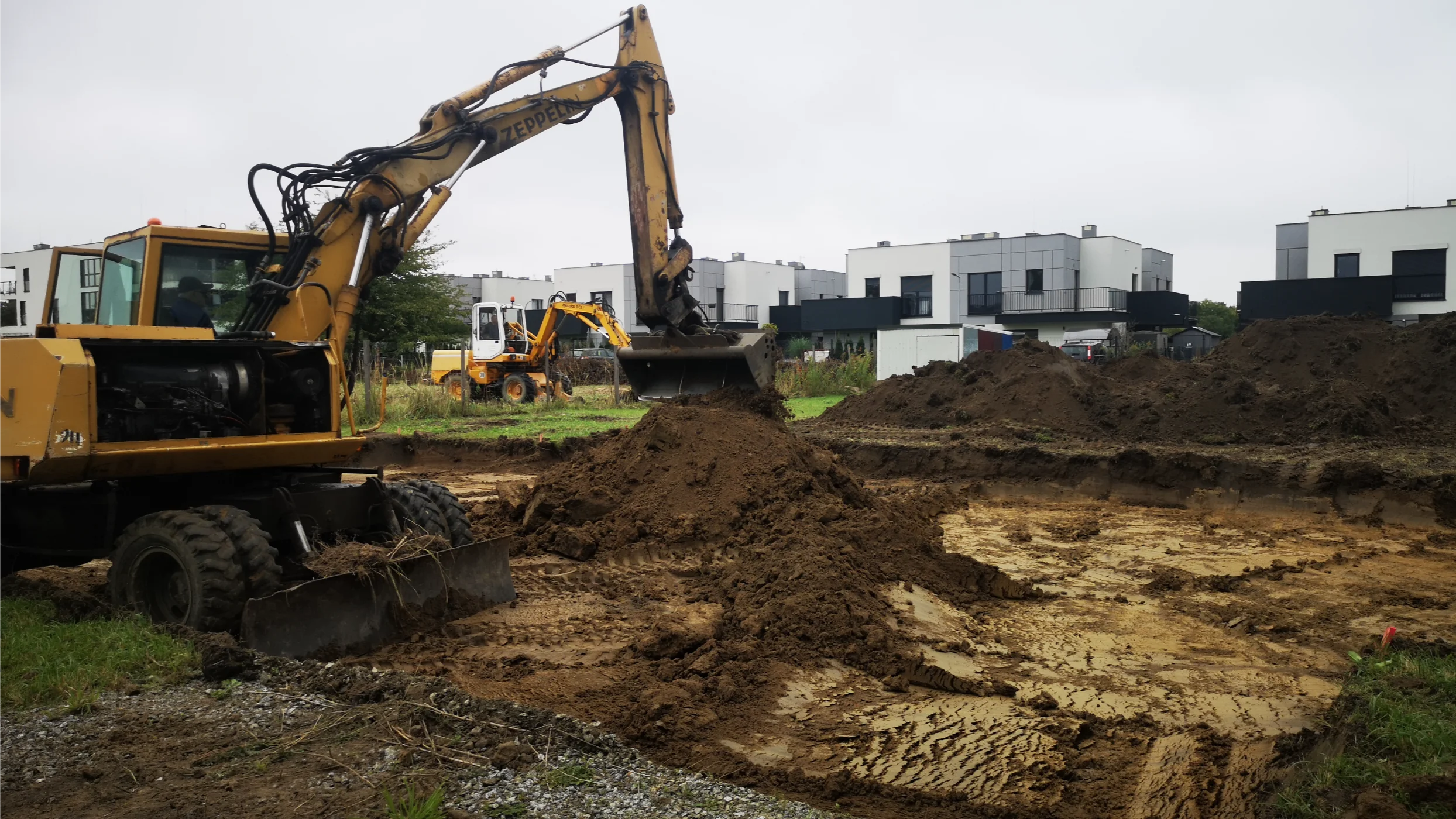 Koparka wykonująca wykop gruntu pod płytę fundamentową na terenie budowy domu